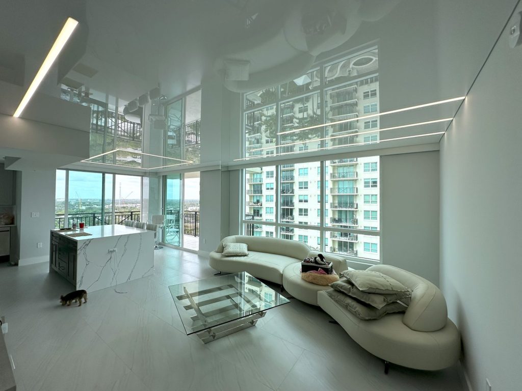 The same living room with a high gloss stretch ceiling and two recessed linear light lines, after